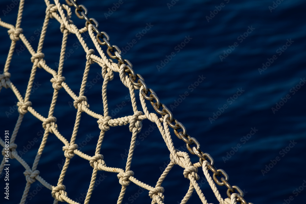 Fototapeta premium Close-up of a nautical net made of rope with a chain link, set against a blue ocean background