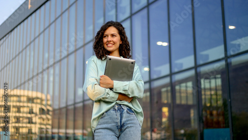 Fotografie Young businesswoman smiling while holding a laptop, standing confidently in fron