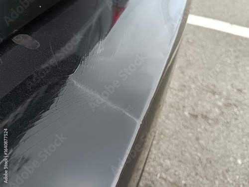 A black car with an old rear bumper, the paint is starting to crack and deteriorate.