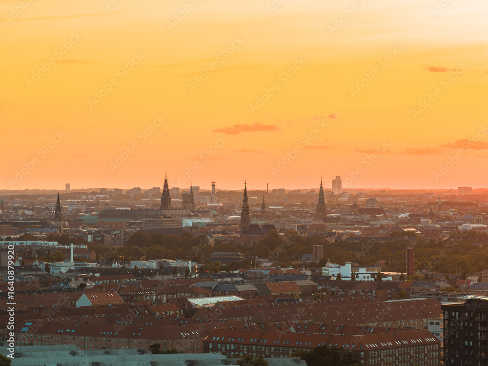 Aerial view of Copenhagen, Denmark, during sunset, featuring historic spires, red roofed buildings, and a mix of modern and traditional architecture. Aerial view of Copenhagen, Denmark, during sunset, featuring historic spires, red roofed buildings, and a mix of modern and traditional architecture.