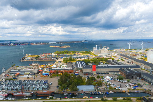 Photography Aerial view of Copenhagen, Denmark, featuring Amager Bakke, wind turbines by the coastline, boats in the harbor, and urban industrial landscapes