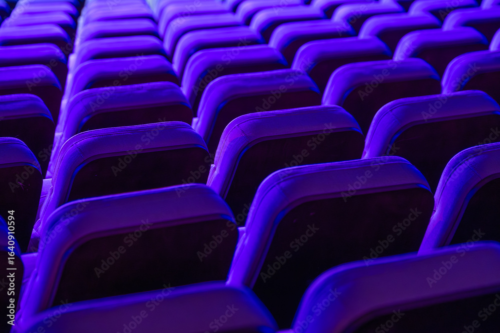 Obraz premium Vibrant rows of theater seats illuminated by purple lights, showcasing repetitiveness and symmetry.