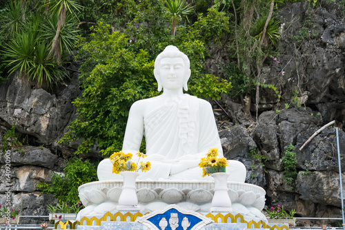 Canvas Print White Buddha statue sitting serenely amidst lush greenery and rocky cliffs in an