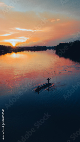 Sunrise fishing on a calm tropical river with wooden canoe.