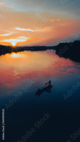 Golden sunrise over serene river fishing scene.