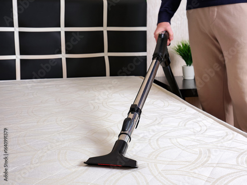 Man disinfecting mattress with vacuum cleaner indoors.. Selective focus.