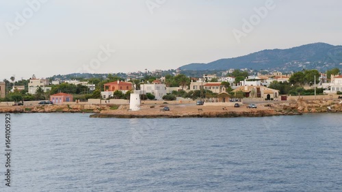 Wallpaper Mural Evening view of Aegina Island with a white lighthouse on a rocky pier, calm sea, coastal houses with tiled roofs, green hillside, and soft sky tones Torontodigital.ca