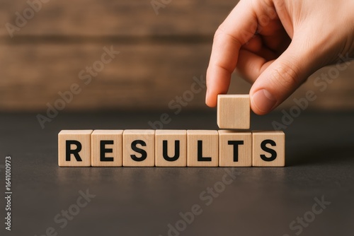 Results Concept: Hand Placing a Wooden Block to Complete the Word Results on Tabletop