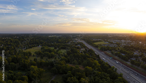 Aerial view of golden light kissing the treetops as cars stream along the highway, painting streaks through the verdant landscape, Charlotte, North Carolina, United States.
