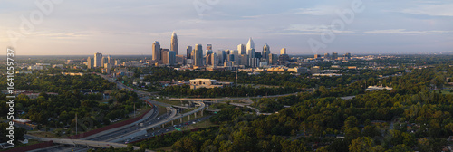Aerial view of a sprawling cityscape with gleaming skyscrapers piercing the horizon, juxtaposed against the lush green canopy and winding highways, Charlotte, North Carolina, United States.