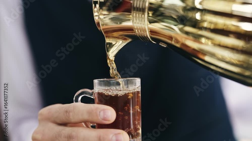 Man carefully pours hot tea from an ornate golden pot into a glass