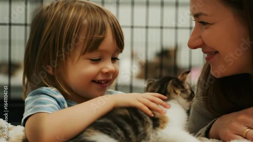 A happy child and their mother gently pet a cute kitten at an animal shelter