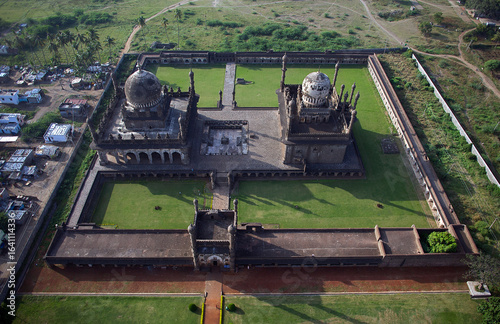 Aerial view of the imposing Gol Gumbaz complex, its dark stone walls contrasting with the vibrant green lawns within, Bijapur, Karnataka, India.