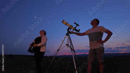 Φωτογραφία Amateur astronomers using telescope and binoculars for watching stars, Moon, planets and other celestial objects from a countryside field in nature