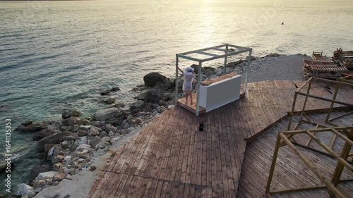 Woman standing on a wooden platform by the sea at sunset