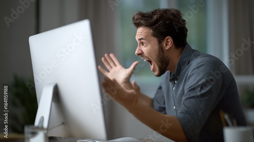 A young man reacts with frustration and anger while looking at his computer screen in a dimly lit room.