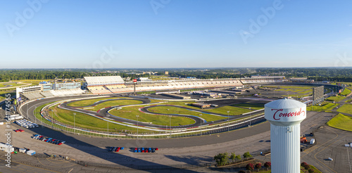 Concord, United States - 28 July 2025: Aerial view of Charlotte Motor Speedway, where the iconic racetrack curves beneath a clear sky, framed by lush greenery and the distinct Concord water tower.
