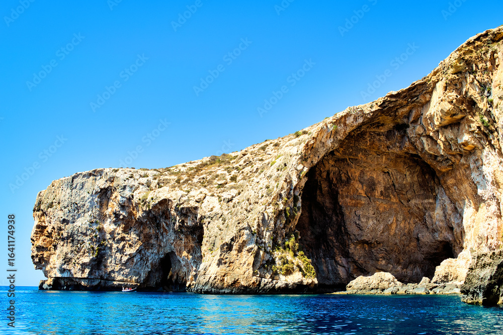 ZURRIEQ, MALTA - Augusts 06, 2021: The Blue Grotto - A famous sea cave surrounded by the deep blue sea at southern Malta. On a traditional boat surrounded by more brightly coloured boats. 