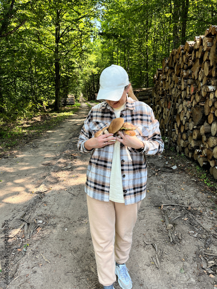 Naklejka premium Happy woman holding basket of wild mushrooms on forest path, eco lifestyle, healthy eating, seasonal harvest.