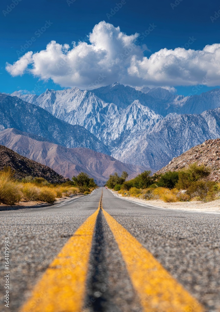 Fototapeta premium Empty road stretching into mountain range. Vast, blue sky, white clouds. Sunny day