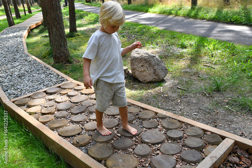 Barefoot boy walking on a sensory trail through a  pine forest