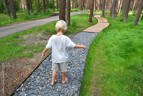Barefoot boy walking on a sensory trail through a pine forest in Lithuania
