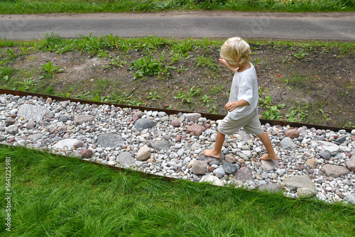 Barefoot boy walking on a sensory trail through a sunny pine forest in summer