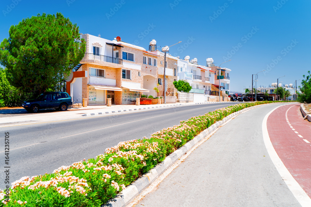 Fototapeta premium Colorful houses in the Mediterranean resort of Polis in Cyprus. Landscape of the island town with an empty road and bike path.