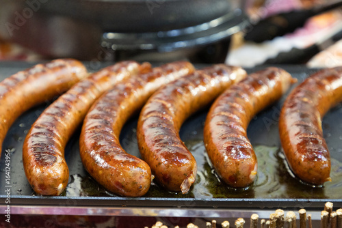 Photos Grilled sausages sizzling on a hot grill with a shiny surface and appetizing gol