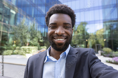 Wallpaper Mural Confident businessman smiles as he takes a selfie, standing outside a contemporary glass office building. Torontodigital.ca
