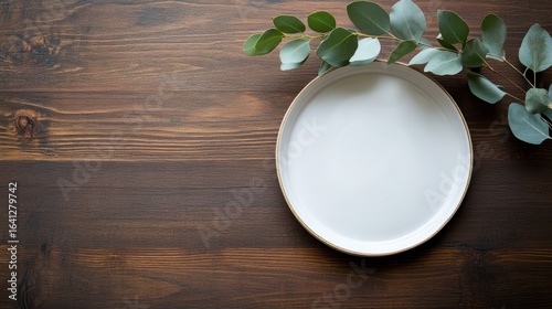 A simple white plate beside green foliage on a wooden surface, creating a minimalist and natural aesthetic.
