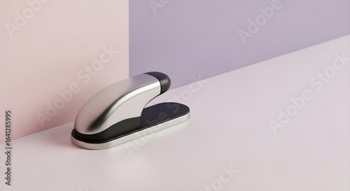 Minimalist silver and black stapler rests on a pale pink surface against a soft purple background