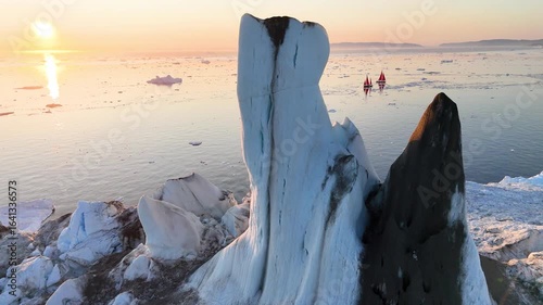 Towering melting iceberg in Arctic icy ocean. Snow covered glacier drift under blue sunny sky. Pure ice floats in turquoise water. Ecology, melting ice, climate change global warming. Aerial view