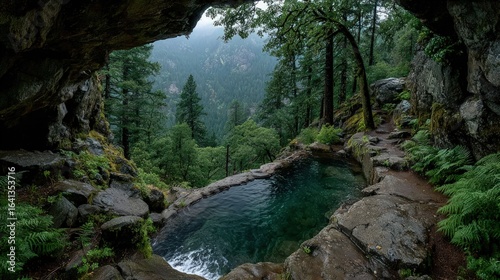 Verdant pool nestled in a rocky mountain overhang, framed by lush forest and misty peaks