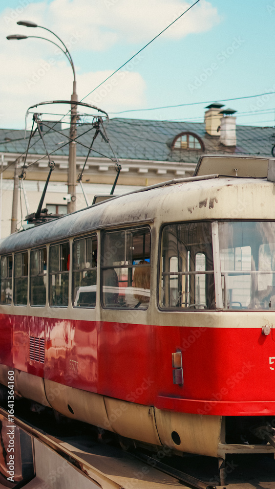 Naklejka premium Red tram arriving at a city tram stop with passengers and urban background