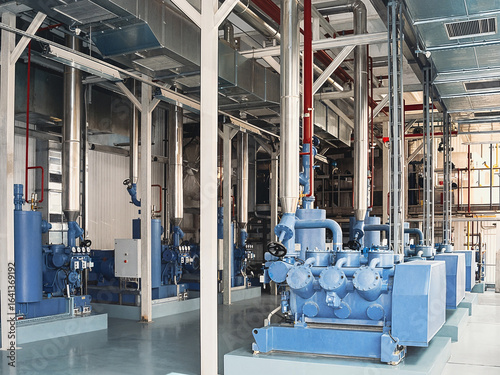 An industrial interior featuring large blue machinery and complex piping systems.
