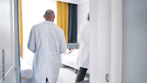 Quadro em tela Two doctors enter the patient's room, view from the back