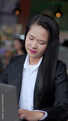 Smiling businesswoman talking on the phone and writing in a notebook with interest, with business district in the background, using phone and apps in the office.