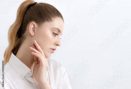 Photograph of beautiful young woman with clean perfect skin in white shirt posing on white background. Portrait of beauty model with natural nude make up. Spa, skincare and wellness