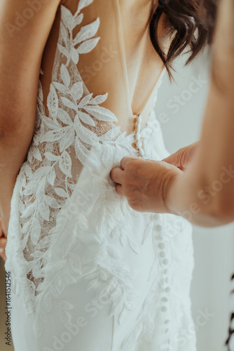 Wedding day morning preparation concept, closeup of bride's mother helping bride fasten white lace wedding dress corset