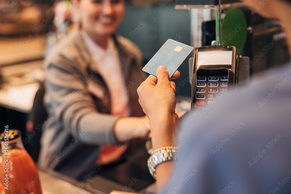 Naklejka premium View from the shoulder of the customer paying by card at pos terminal in a grocery store