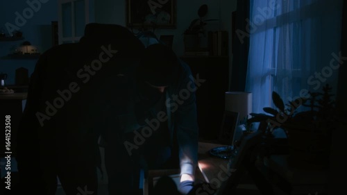 Two unrecognizable thieves in black balaclavas rummaging through drawer in living room during break in while police arriving