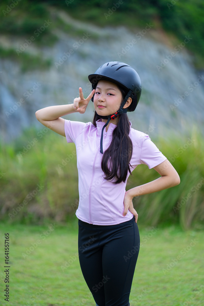 Young girl wearing helmet poses confidently outdoors, showing peace sign with playful expression Young girl wearing helmet poses confidently outdoors, showing peace sign with playful expression