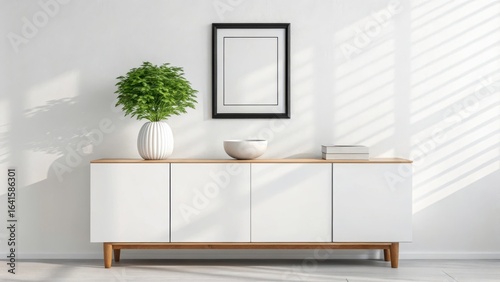 Modern white sideboard with wooden legs displaying a green plant in a vase and framed artwork on a wall