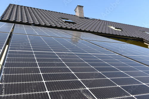 Close-up of photovoltaic panels installed on a house roof, with rural landscape in the background on a sunny summer day