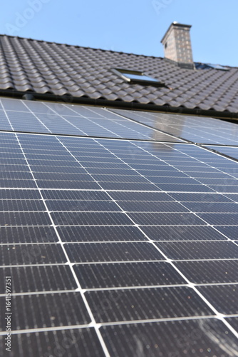 Close-up of photovoltaic panels installed on a house roof, with rural landscape in the background on a sunny summer day