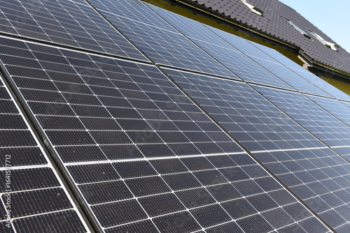 Close-up of photovoltaic panels installed on a house roof, with rural landscape in the background on a sunny summer day