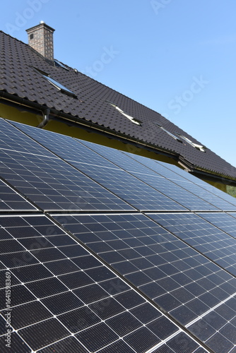 Close-up of photovoltaic panels installed on a house roof, with rural landscape in the background on a sunny summer day