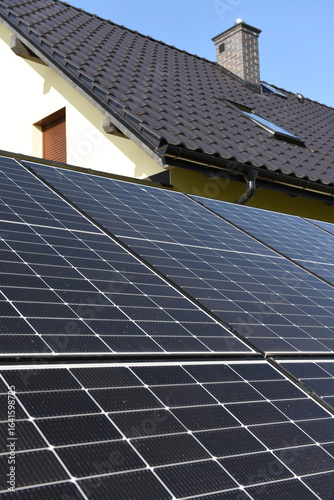 Close-up of photovoltaic panels installed on a house roof, with rural landscape in the background on a sunny summer day