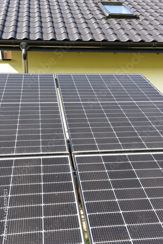 Close-up of photovoltaic panels installed on a house roof, with rural landscape in the background on a sunny summer day